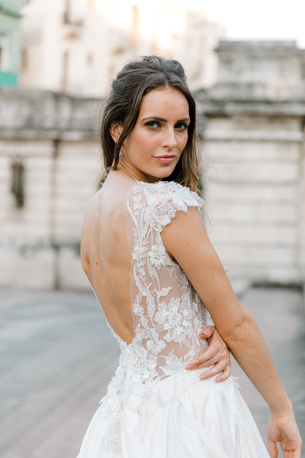 Model wearing Vinka Design Annalie Wedding Dress, a Beaded Lace High Neck Silk Wedding Gown close up facing away showing low back detail in the backdrop of Havana