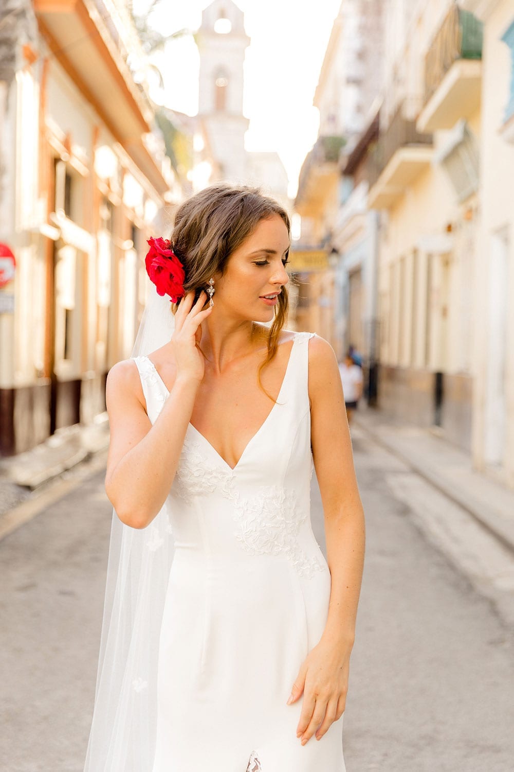 Model wearing Vinka Design Carmen Wedding Dress, a V Neck A-Line Wedding Gown worn on the streets of Havana close up with a flower in her hair
