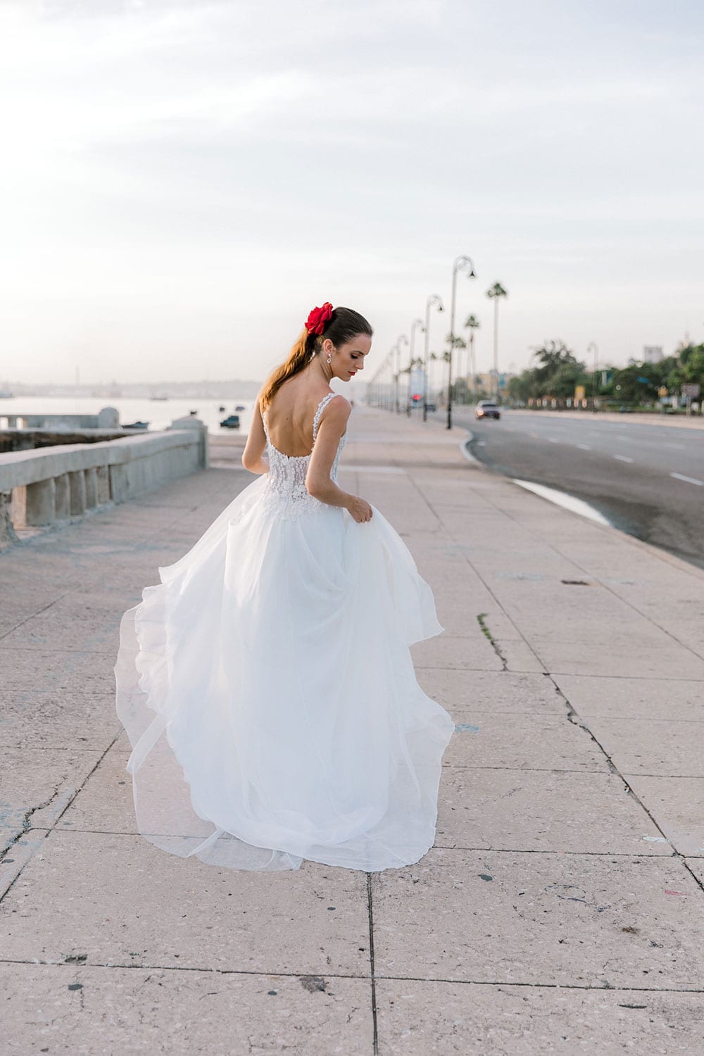 Model wearing Vinka Design Iris Wedding Dress, a Silk Chiffon Wedding Gown posed on a paved walkway in Havana walking away with dress flowing