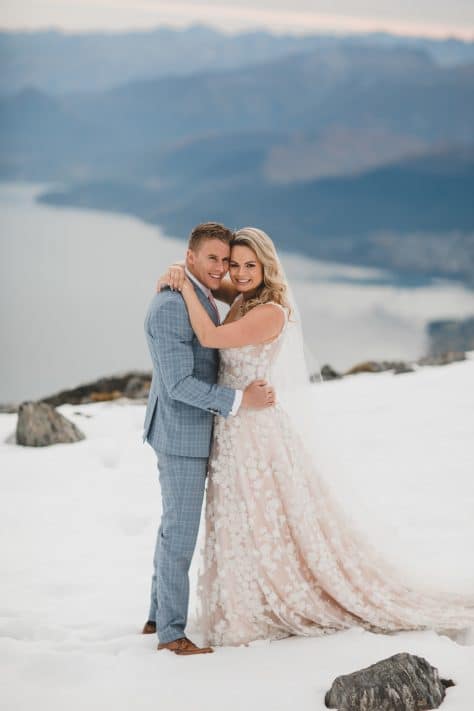 Real Weddings | Vinka Design | Real Brides Wearing Vinka Gowns | Megan and Tim together on a mountain top in Queenstown custom made dress train flowing behind Megan