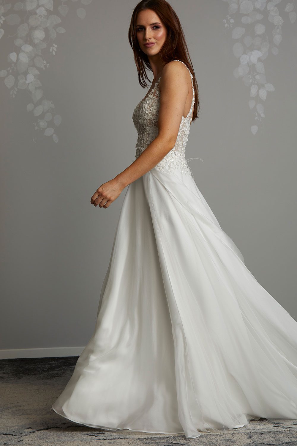 Iris Wedding Dress from Vinka Design. Soft and feminine, this gown has beautiful movement, with the silk chiffon making the design very light and fluid. The boned bodice is semi-sheer and is highlighted by delicate 3-D beaded flower lace. Profile of Model wearing silk chiffon gown with 3D floral lace