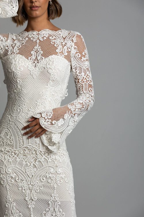 Sabine Wedding Dress from Vinka Design. This gorgeous gown is made with a delicate French crocheted lace, which falls with a real softness. It has a stretch base to fit curves to perfection, and also features a low back and incredible long lace sleeves. Close up of front of dress with high neckline, long sleeves and long skirt made with beautiful French crochet lace