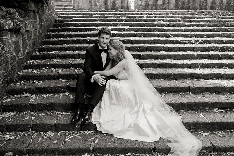 Testimonials | Vinka Design | Real Bridal Reviews from Our Clients | Anna and husband on stone steps with designer dress flowing down