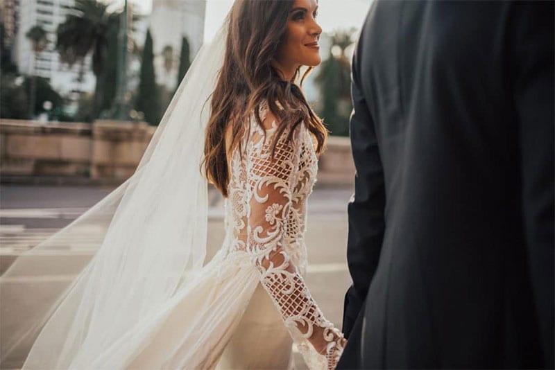 Testimonials | Vinka Design | Real Bridal Reviews from Our Clients | Hannah and Campbell walking along side view of stunning lace detail on nude base of dress bodice prominent