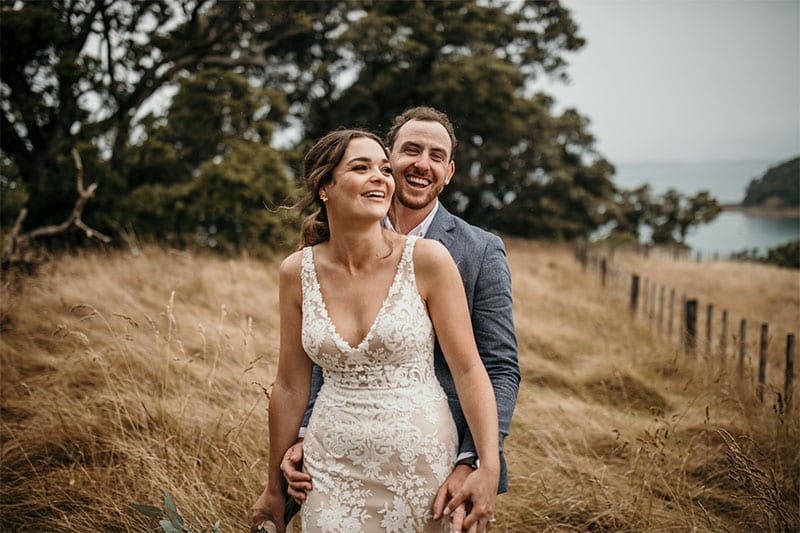 Testimonials | Vinka Design | Real Bridal Reviews from Our Clients | Melissa and Aaron in field with lace front detail and v neck of beautiful bespoke gown featured