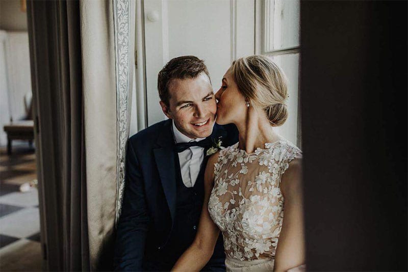 Testimonials | Vinka Design | Real Bridal Reviews from Our Clients | Paige and husband seated with lace bodice of bespoke gown highlighted