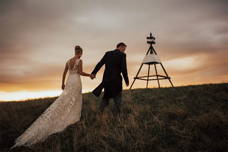 Testimonials | Vinka Design | Real Bridal Reviews from Our Clients | Sarah and Alex walk up hill with bespoke gown flowing behind