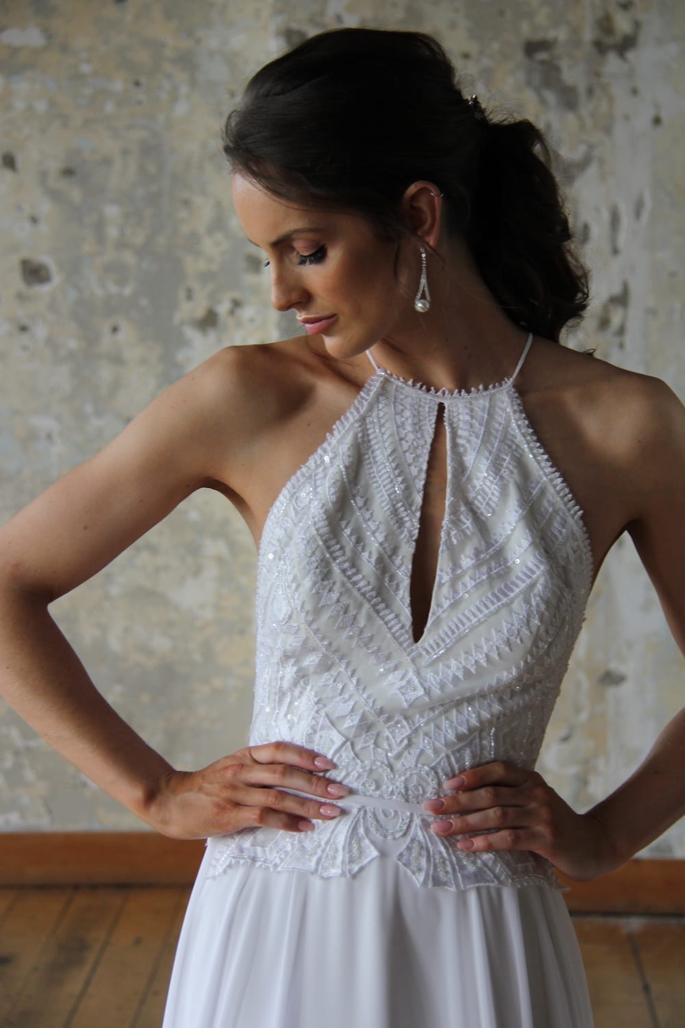 Female model wearing Vinka Design Modern Muse Wedding Dress. In chic warehouse the front detail of a light, halter-necked gown with a fluid chiffon skirt.