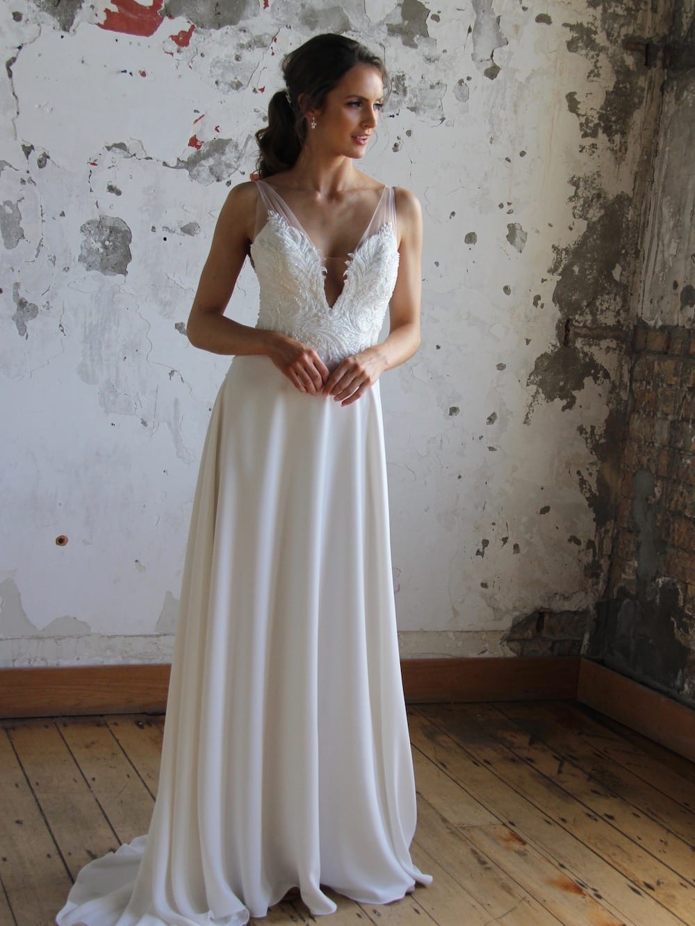 Female model wearing Vinka Design Modern Muse Wedding Dress. In chic warehouse the front detail of a gown with beaded lace and tulle bodice and bridal crepe skirt with train.