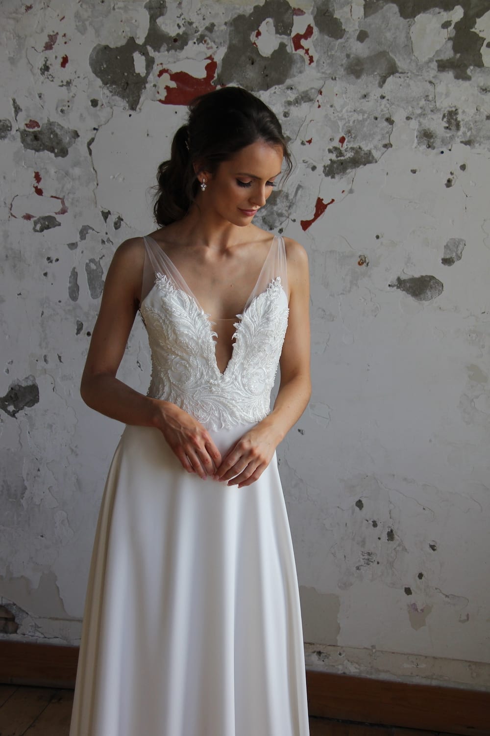 Female model wearing Vinka Design Modern Muse Wedding Dress. In chic warehouse the front detail of a gown with beaded lace and tulle bodice and bridal crepe skirt with train.