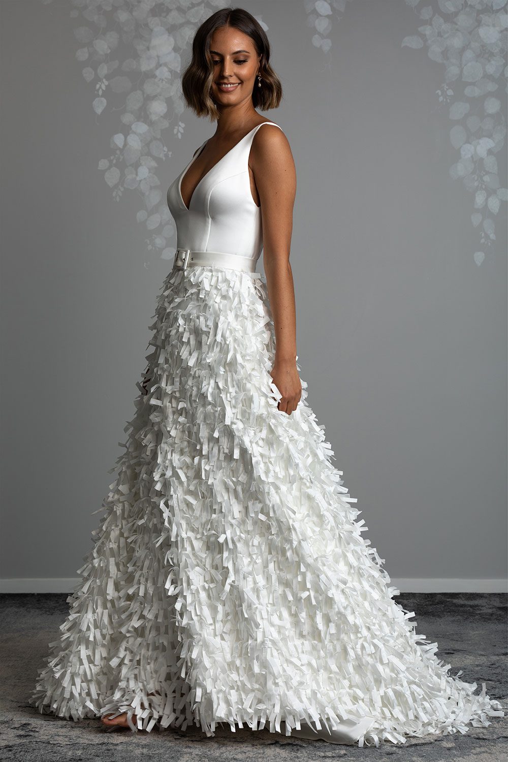 Bianca wedding dress from Vinka design. Model wearing deep V cut dress with belt and ribbon cut skirt