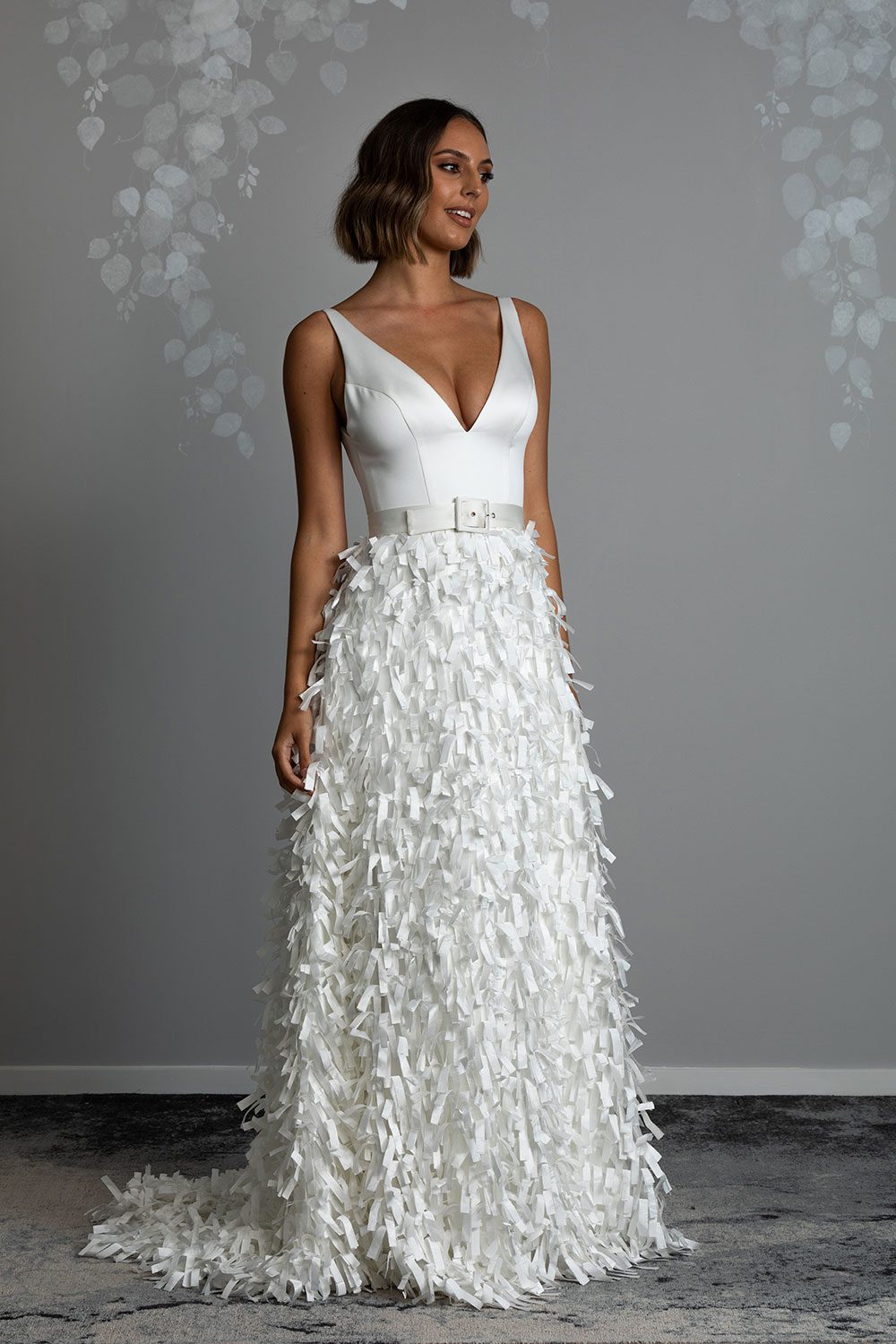 Bianca wedding dress from Vinka design. Full length view of model looking over shoulder of deep V cut dress with ribbon cut satin skirt
