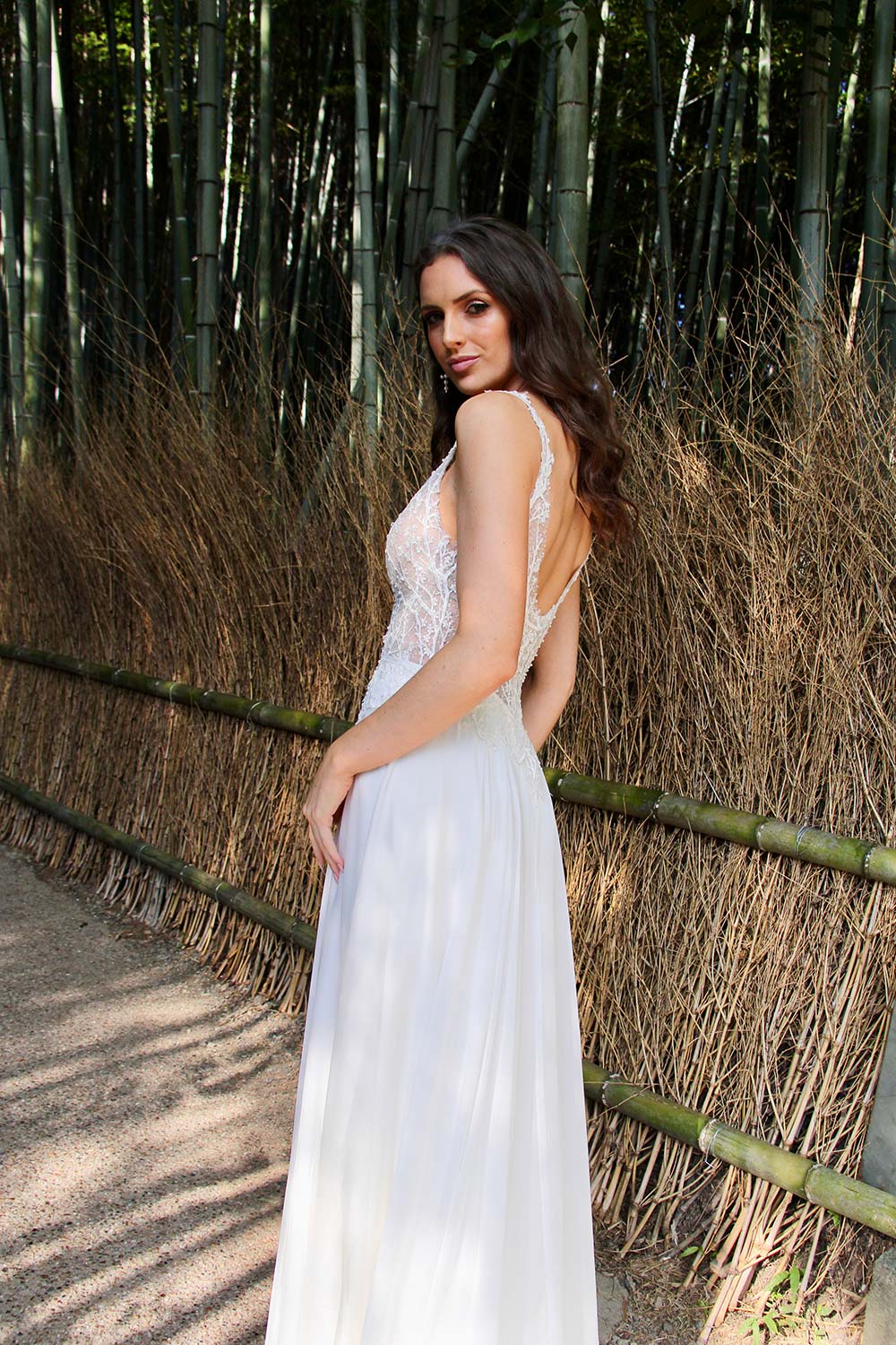 Female model wearing Vinka Design An Oriental Affair Wedding Dress. In a Japanese bamboo forest the side detail of a gown with a bodice of two beaded laces on a nude base and a silk chiffon skirt with side split.
