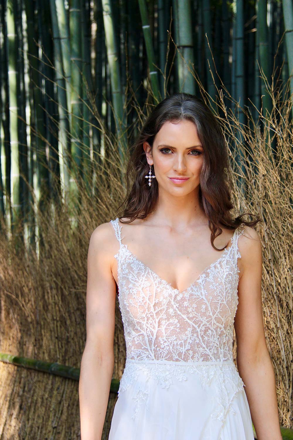 Female model wearing Vinka Design An Oriental Affair Wedding Dress. In a Japanese bamboo forest the front detail of a gown with a bodice of two beaded laces on a nude base and a silk chiffon skirt with side split.