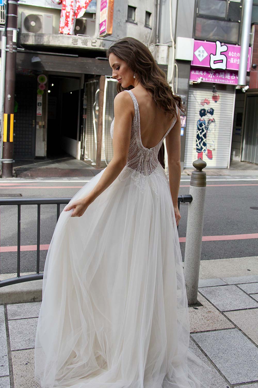 Female model wearing Vinka Design An Oriental Affair Wedding Dress. On a Japanese street the front detail of a gown with a hand-beaded, nude-based, semi sheer bodice with a deep v-neckline and low back with a tulle skirt.