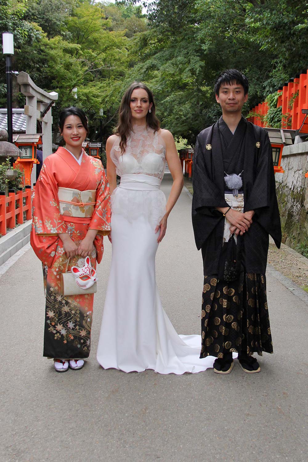 Female model wearing Vinka Design An Oriental Affair Wedding Dress. Standing in a gothic doorway the front detail of gown with a high necked delicately hand-embroidered leaf lace cinched in at the waist with a wide kimono belt with skirt