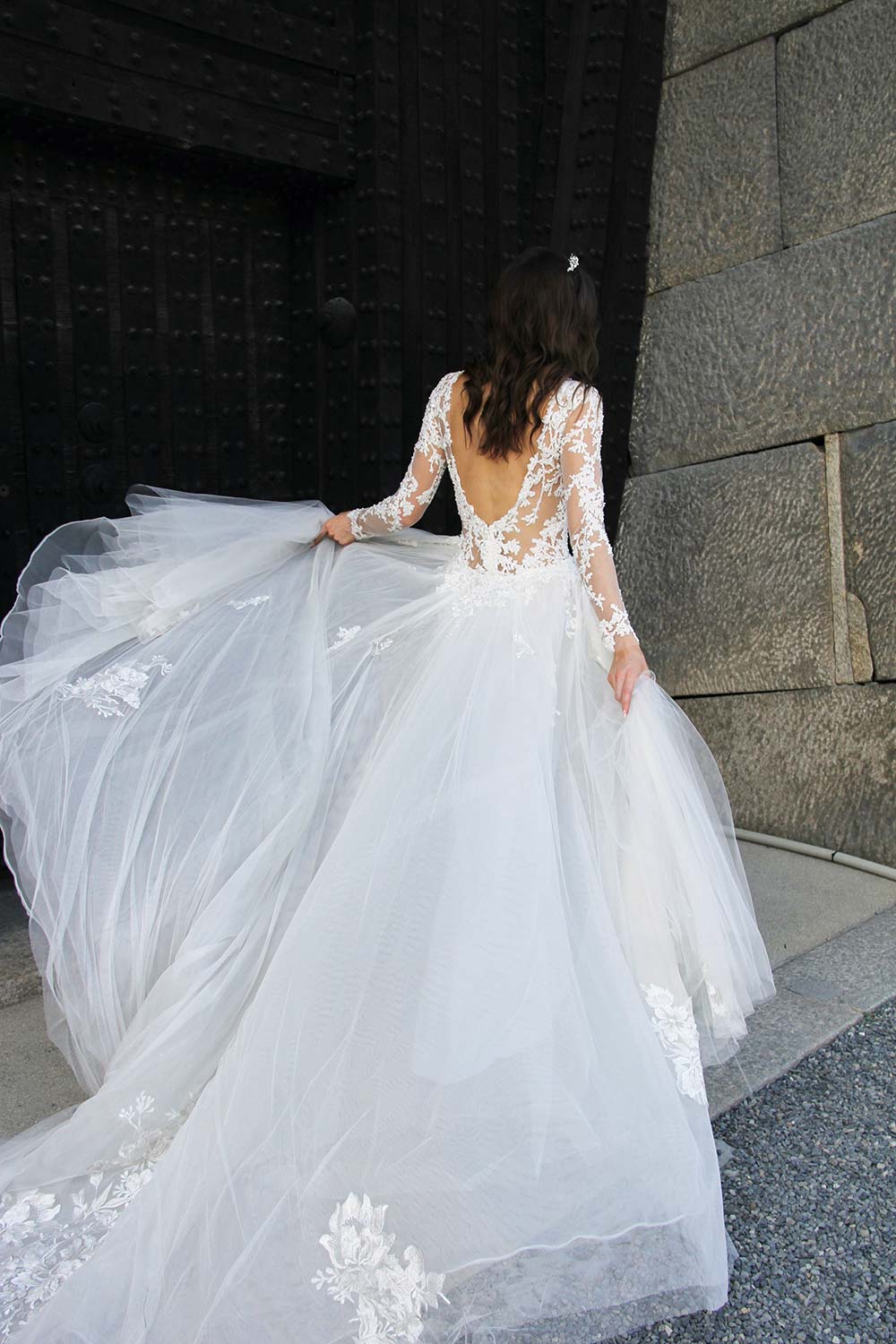 Female model wearing Vinka Design An Oriental Affair Wedding Dress. Standing in a gothic doorway the back detail of gown with a high neckline and a daringly low back and a flattering floor-length detachable skirt