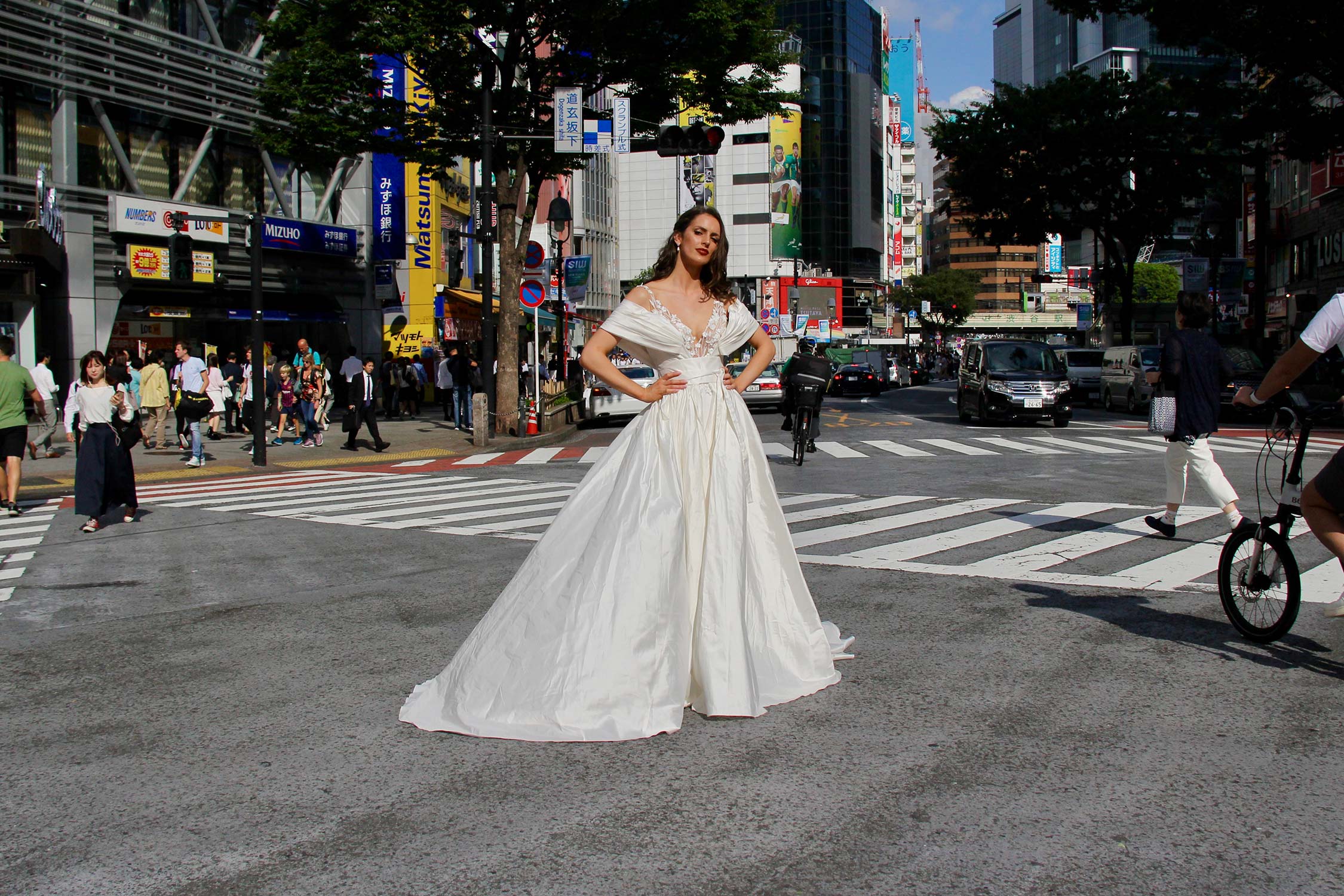 Female model wearing Vinka Design An Oriental Affair Wedding Dress. In a busy japanese crossing the front detail of a three-dimensional beaded flower lace gown on a nude base with a kimono over-dress and slim fitting floor length skirt.