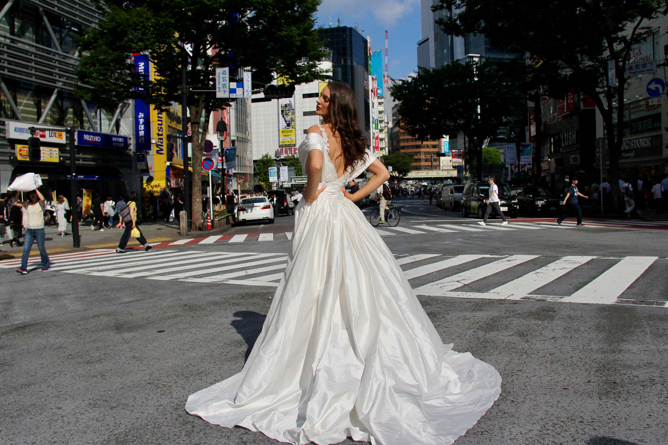 Female model wearing Vinka Design An Oriental Affair Wedding Dress. In a busy japanese crossing the back detail of a three-dimensional beaded flower lace gown on a nude base with a kimono over-dress and slim fitting floor length skirt.