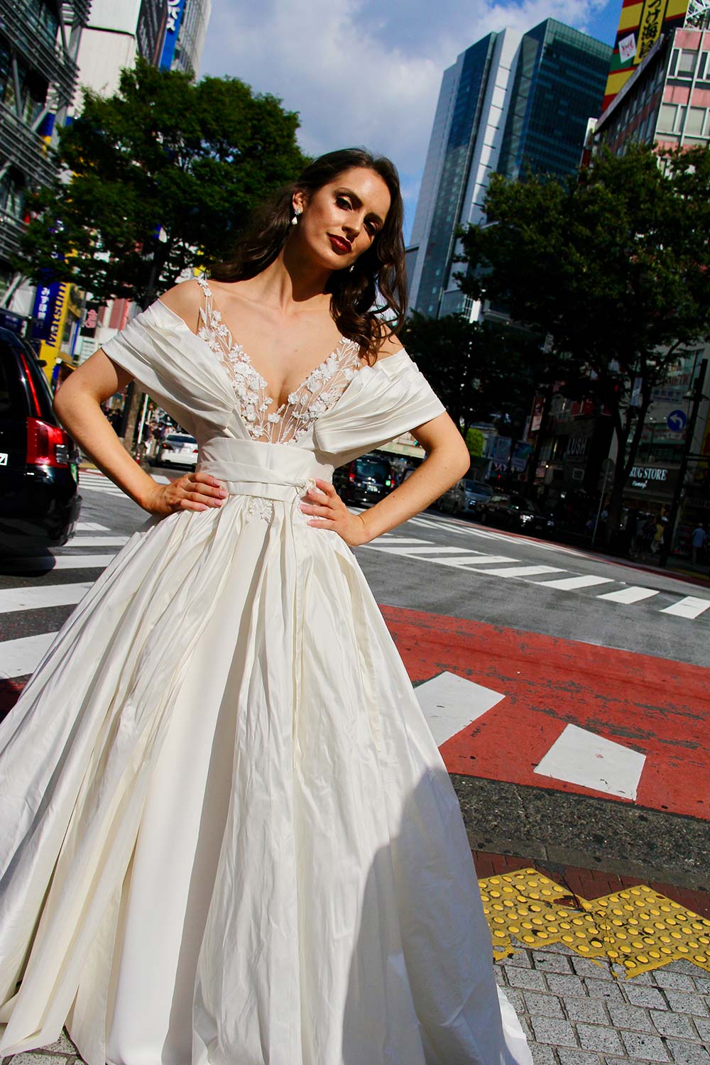 Female model wearing Vinka Design An Oriental Affair Wedding Dress. In a busy japanese crossing the front detail of a three-dimensional beaded flower lace gown on a nude base with a kimono over-dress and slim fitting floor length skirt.