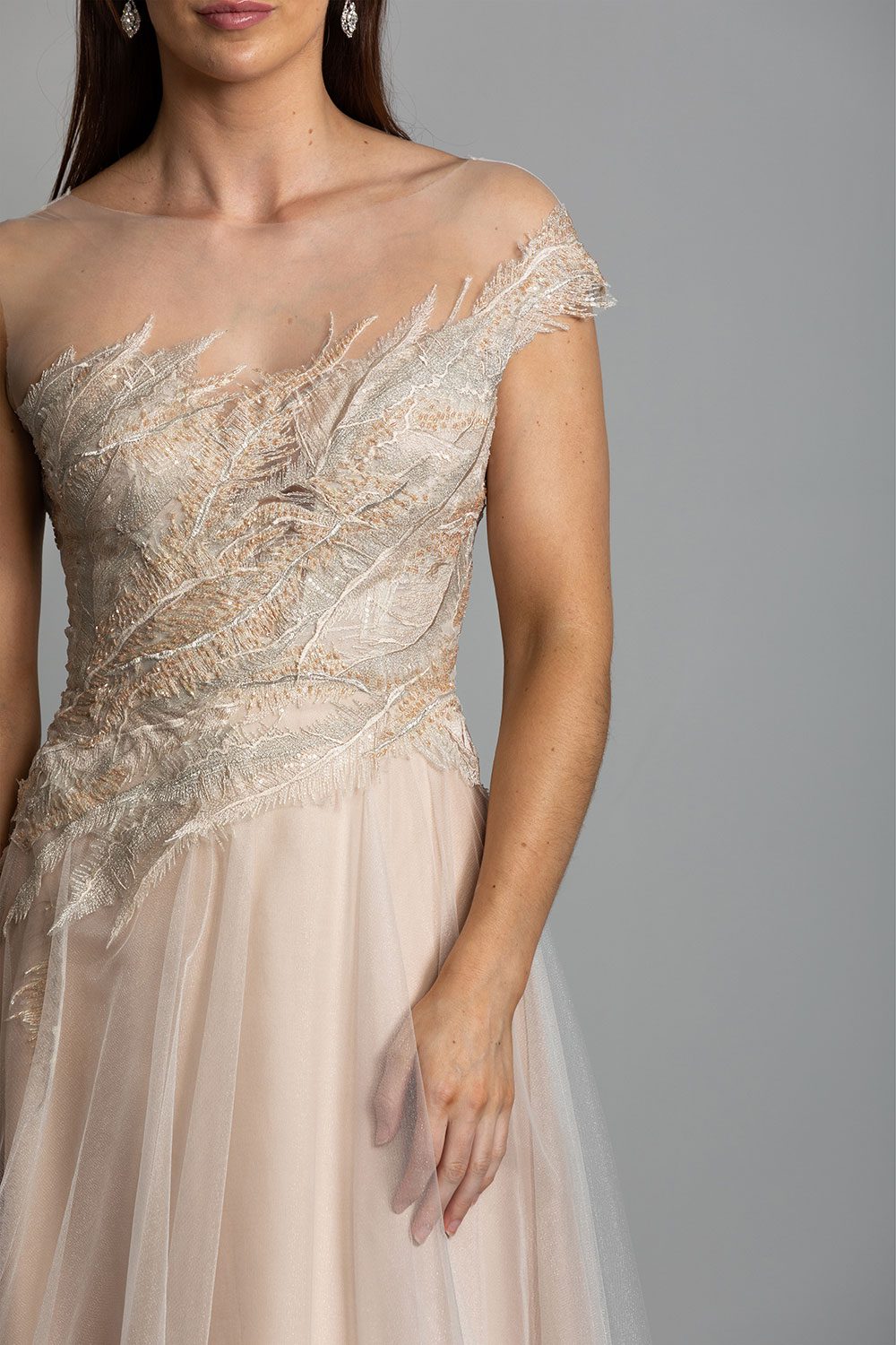 Takara Wedding Dress from Vinka Design. This glorious A-line gown is a wonderland vision in blush. Featuring a dreamscape of luxe, intricately embroidered beaded feather lace, and layers of dreamy, soft gold tulle on a blush silk organza base. Close up of model wearing beaded feather lace bodice with one shoulder detail and soft gold tulle skirt