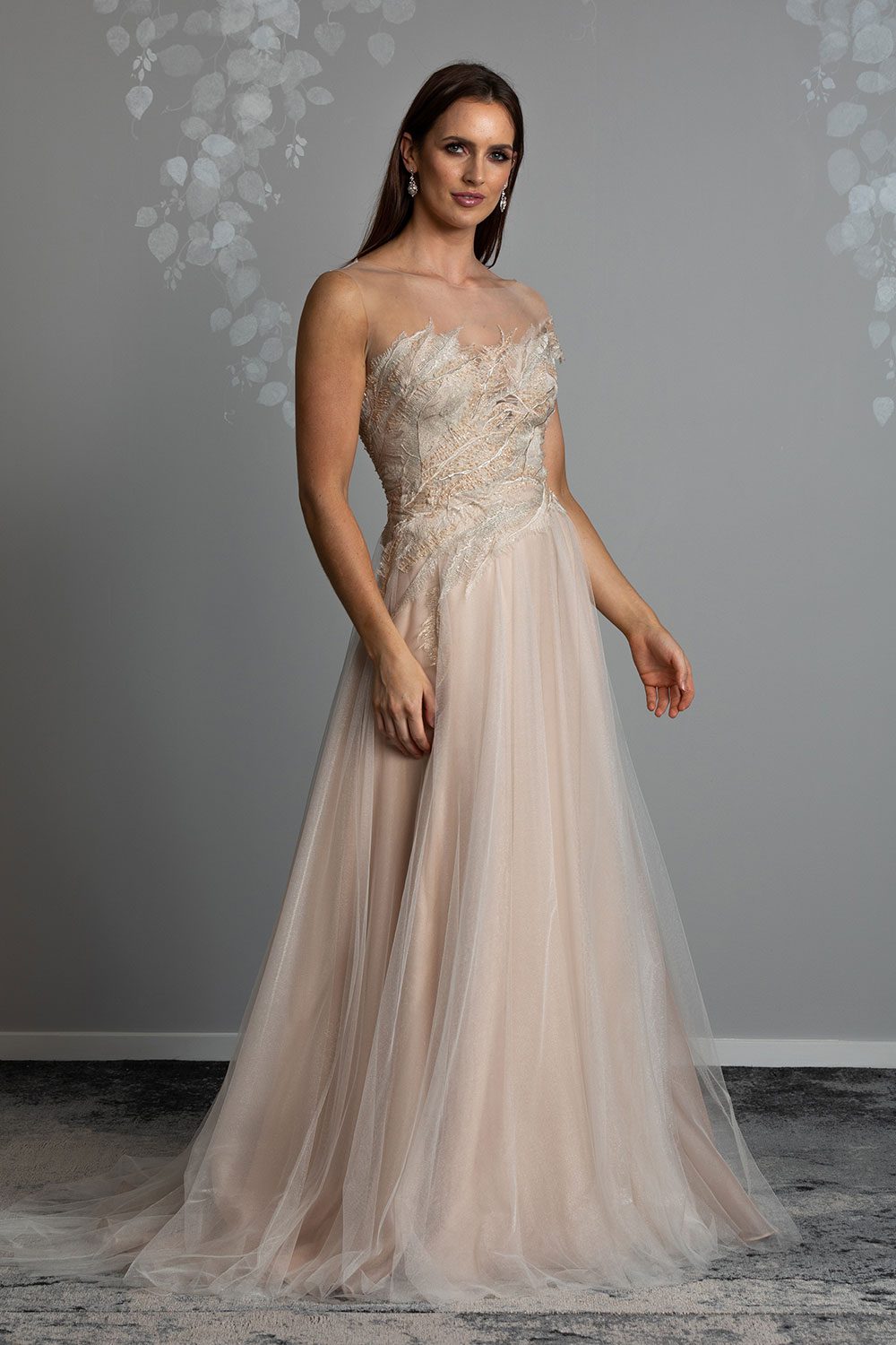 Takara Wedding Dress from Vinka Design. This glorious A-line gown is a wonderland vision in blush. Featuring a dreamscape of luxe, intricately embroidered beaded feather lace, and layers of dreamy, soft gold tulle on a blush silk organza base. Full length view of model wearing beautiful feather beaded lace gown with soft gold tulle skirt