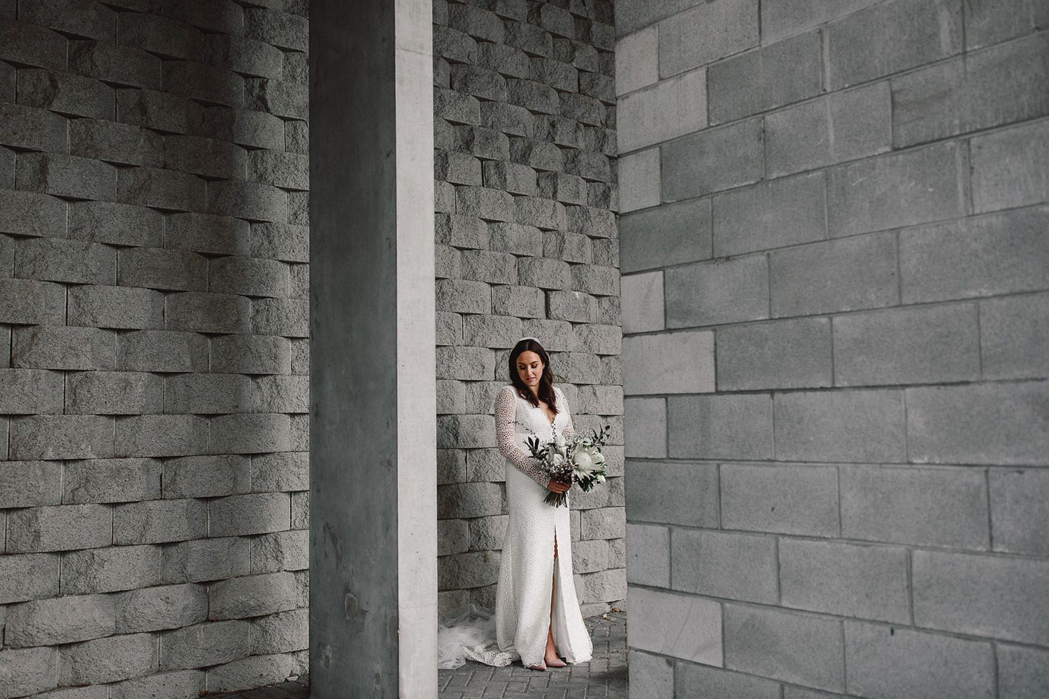 Vinka Design Features Real Weddings - bride in custom made gown fitted with a deep V neckline, front split and long lace sleeves. In big grey brick building