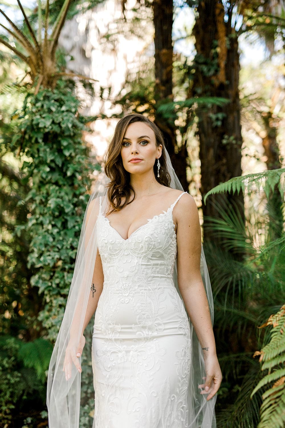 Sahara Wedding Dress from Vinka Design. Stunning fitted lace wedding gown. Lightly-beaded floral lace highlights the ivory stretch satin base. Sweetheart neckline & low back with beautiful lace detail. Detail of top of dress. Photographed in landscaped gardens.