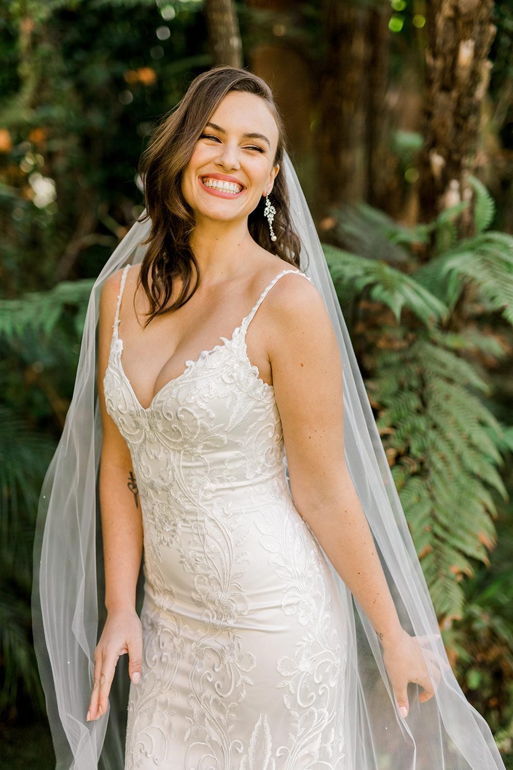Sahara Wedding Dress from Vinka Design. Stunning fitted lace wedding gown. Lightly-beaded floral lace highlights the ivory stretch satin base. Sweetheart neckline & low back with beautiful lace detail. Front of dress. Photographed in landscaped gardens.
