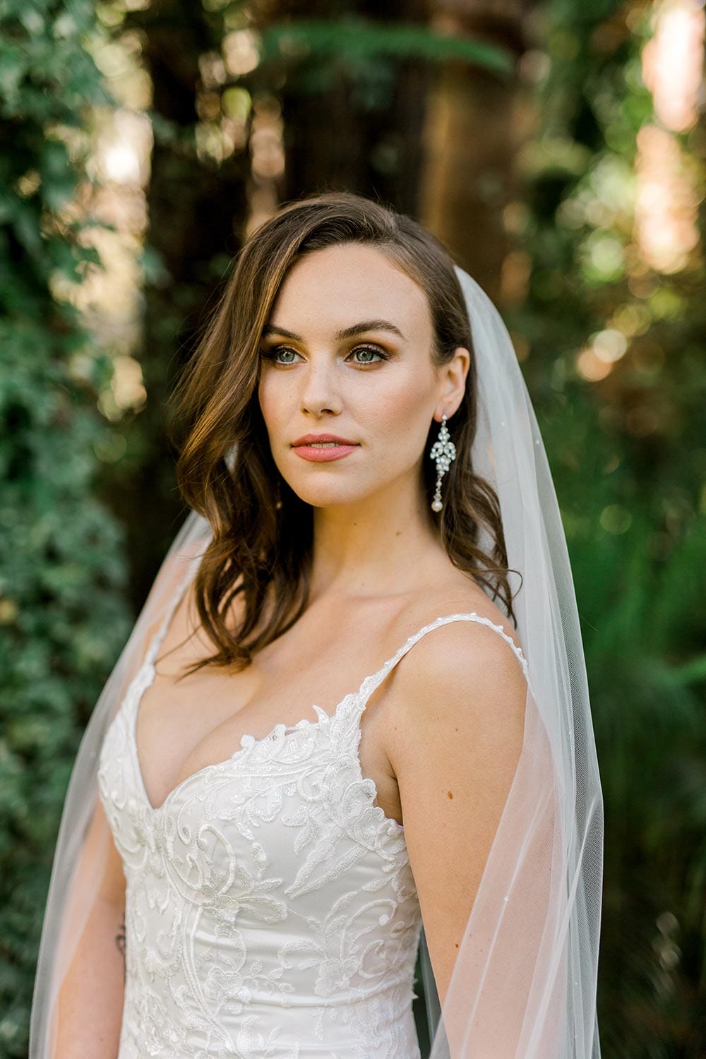 Sahara Wedding Dress from Vinka Design. Stunning fitted lace wedding gown. Lightly-beaded floral lace highlights the ivory stretch satin base. Sweetheart neckline & low back with beautiful lace detail. Front of dress with neckline. Photographed in landscaped gardens.