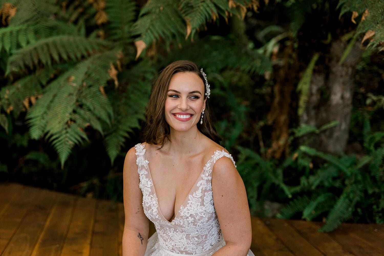 Vivian Wedding gown from Vinka Design - A stunning gown with a deep V-neckline on both the front & back. Fitted semi-sheer nude bodice embellished with a beaded floral lace, a soft layered tulle skirt. Worn in conservatory with fern background, close up of top.