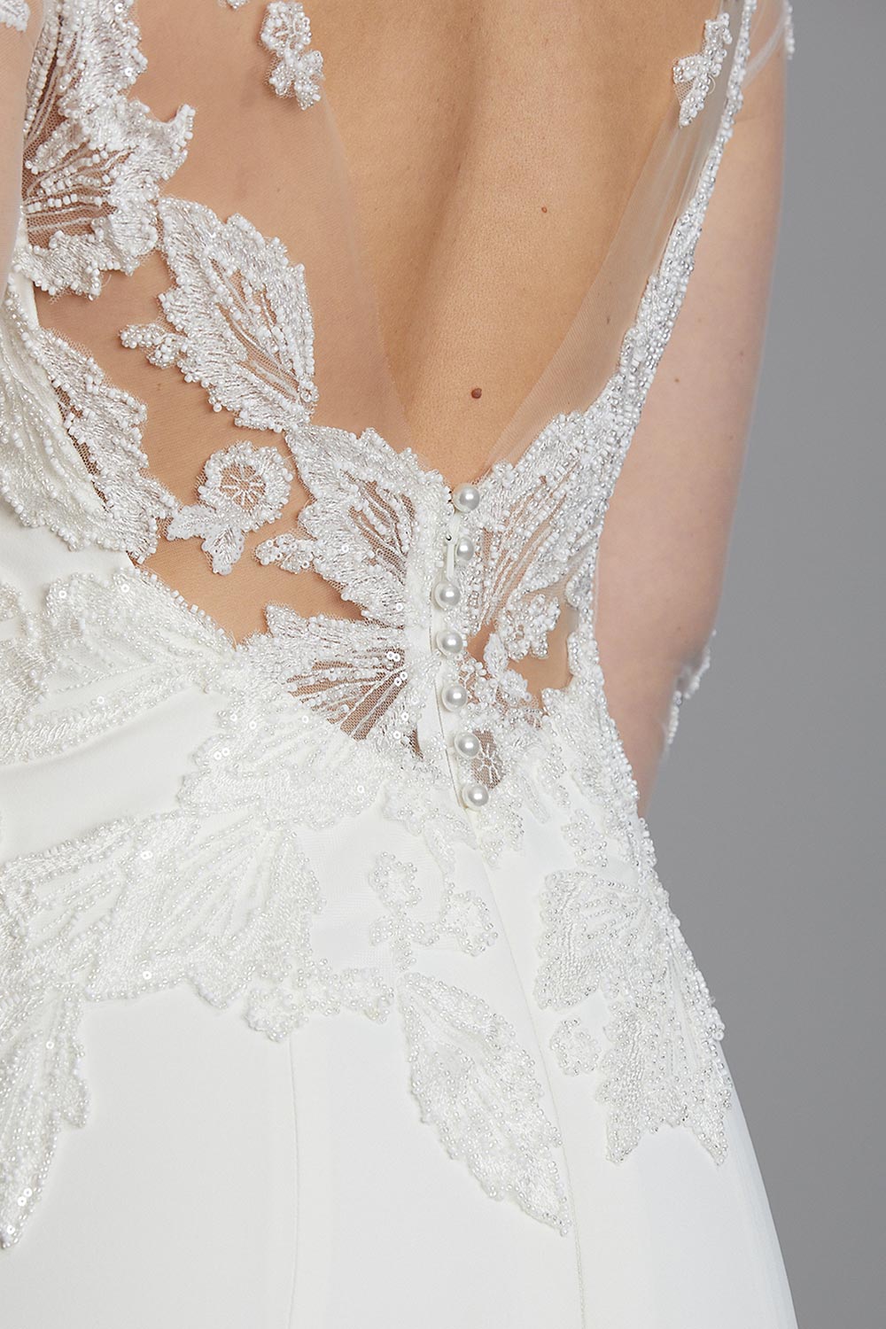 Ariel Wedding Dress from Vinka Design. Wedding dress with illusion scoop neckline & sheer low back with beaded lace. Long, fitted lace sleeves with pearl buttons & A-line skirt that falls into a train. Close up of low back lace detail of the dress, photographed by Emmaline Photography.