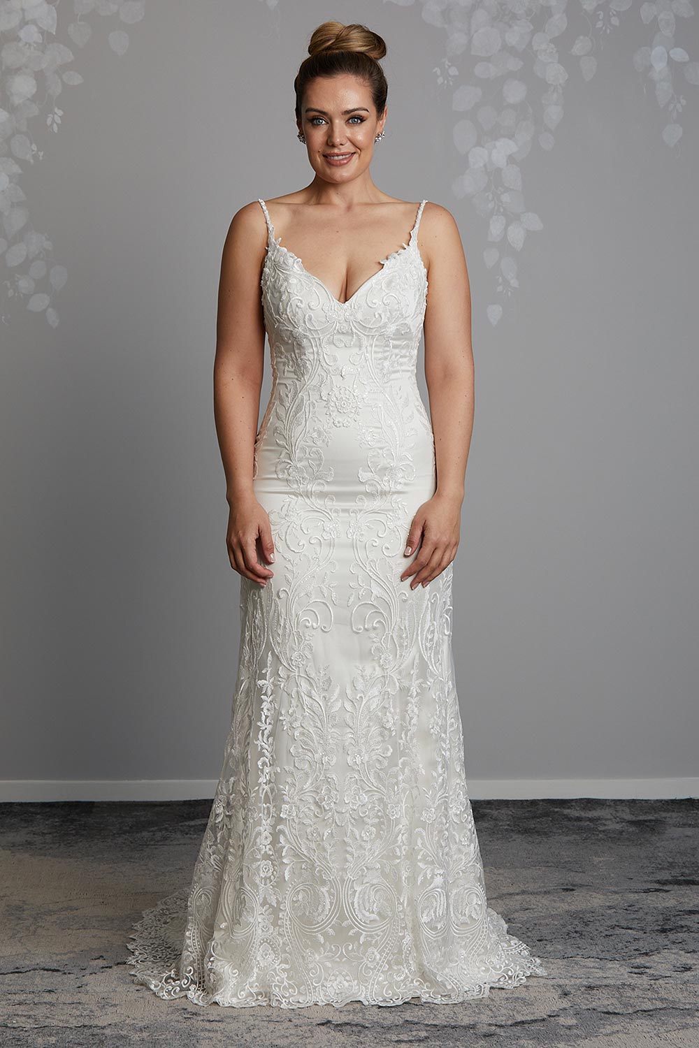Sahara Wedding Dress from Vinka Design. Stunning fitted lace wedding gown. Lightly-beaded floral lace highlights the ivory stretch satin base. Sweetheart neckline & low back with beautiful lace detail. Full length view of the front of the dress as model smiles.
