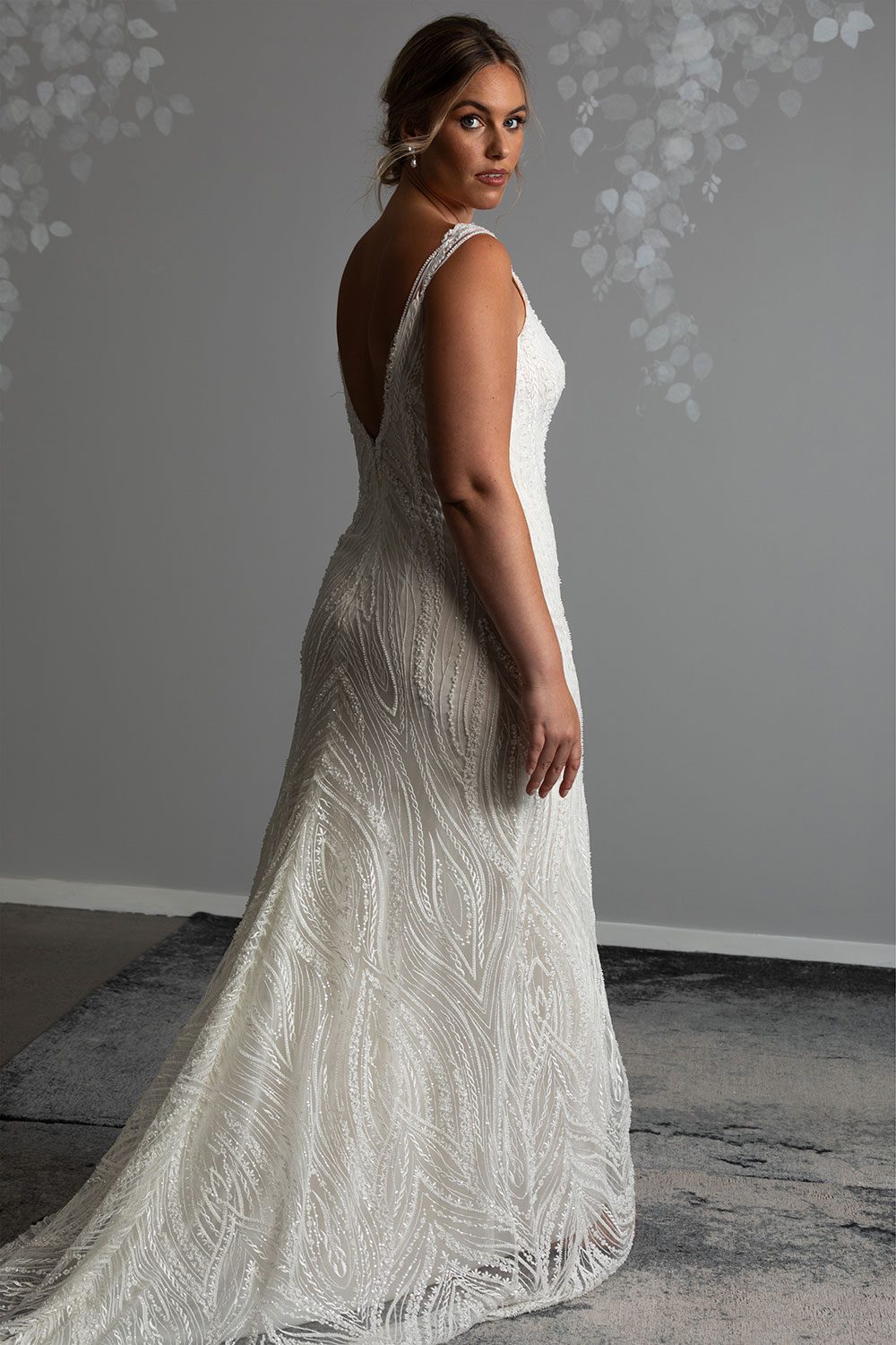 Kiera Wedding Dress from Vinka Design. Beautifully beaded lace wedding dress. Deep V-neckline both front and back is complemented with delicate sheer lace shoulder detail & structured bodice. Model showing back of dress with beautiful beaded lace