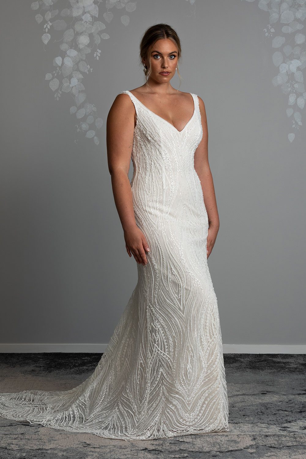 Kiera Wedding Dress from Vinka Design. Beautifully beaded lace wedding dress. Deep V-neckline both front and back is complemented with delicate sheer lace shoulder detail & structured bodice. Model showing front of the dress with deep V-neckline and beaded ivory lace over a champagne base
