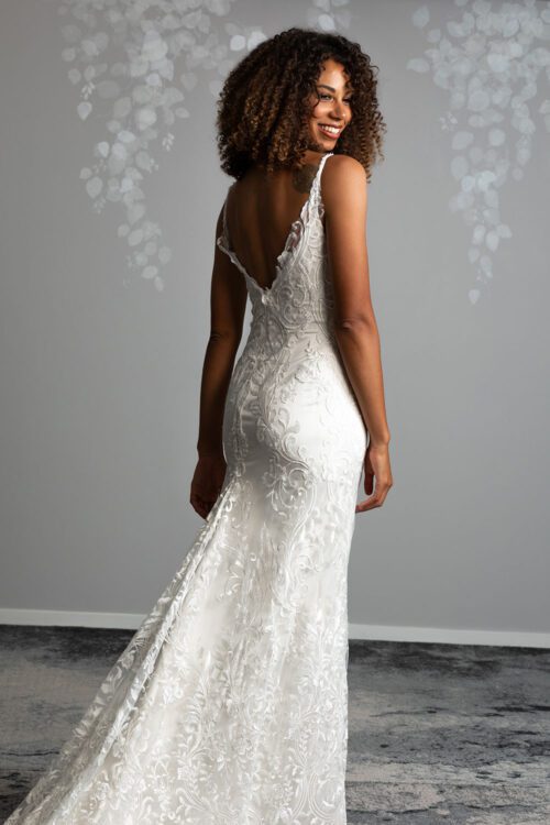 Sahara Wedding Dress from Vinka Design. Stunning fitted lace wedding gown. Lightly-beaded floral lace highlights the ivory stretch satin base. Sweetheart neckline & low back with beautiful lace detail. Model looking back over shoulder showcasing low back gown with long lace train