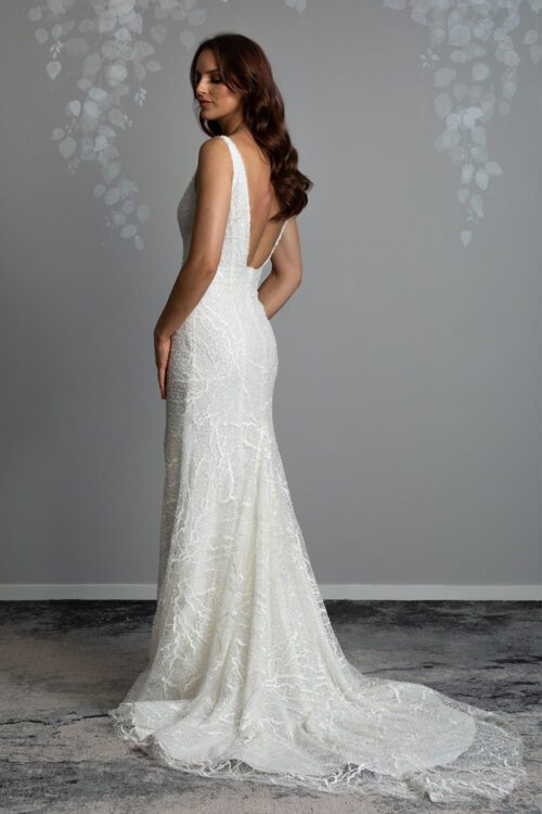 Farrah Wedding gown from Vinka Design - This beautiful wedding dress is constructed with fully beaded embroidered lace on a stretch base. V-neckline with a low, square back cut in a fit-and-flare style, which gently sculpts and enhances curves. Model showing back view of dress with low square back detail and long beaded embroidered train