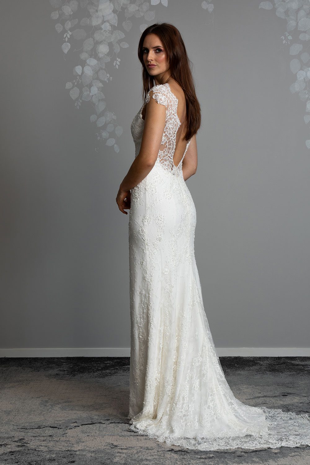 Fallyn Wedding gown from Vinka Design - This wedding dress is a timeless classic. Dramatic scallop lace and deep V-shaped neckline with beautiful low back and mini cap sleeves. This gown is cut in a fit-and-flare design with a side split. Full length view of back of gown with long train and beautiful scallop lace across low cut back