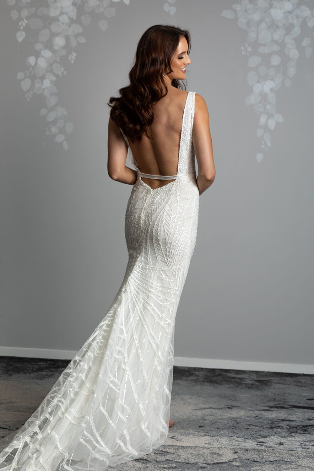 Elle Wedding gown from Vinka Design - Wedding dress with illusion neckline and deep plunge in the front with low back. Stunning beaded embroidery over a stretch base that sculpts and flatters the figure and falls into a beautiful flared train. Back view of dress showing low back with beaded strap and stunning flared train