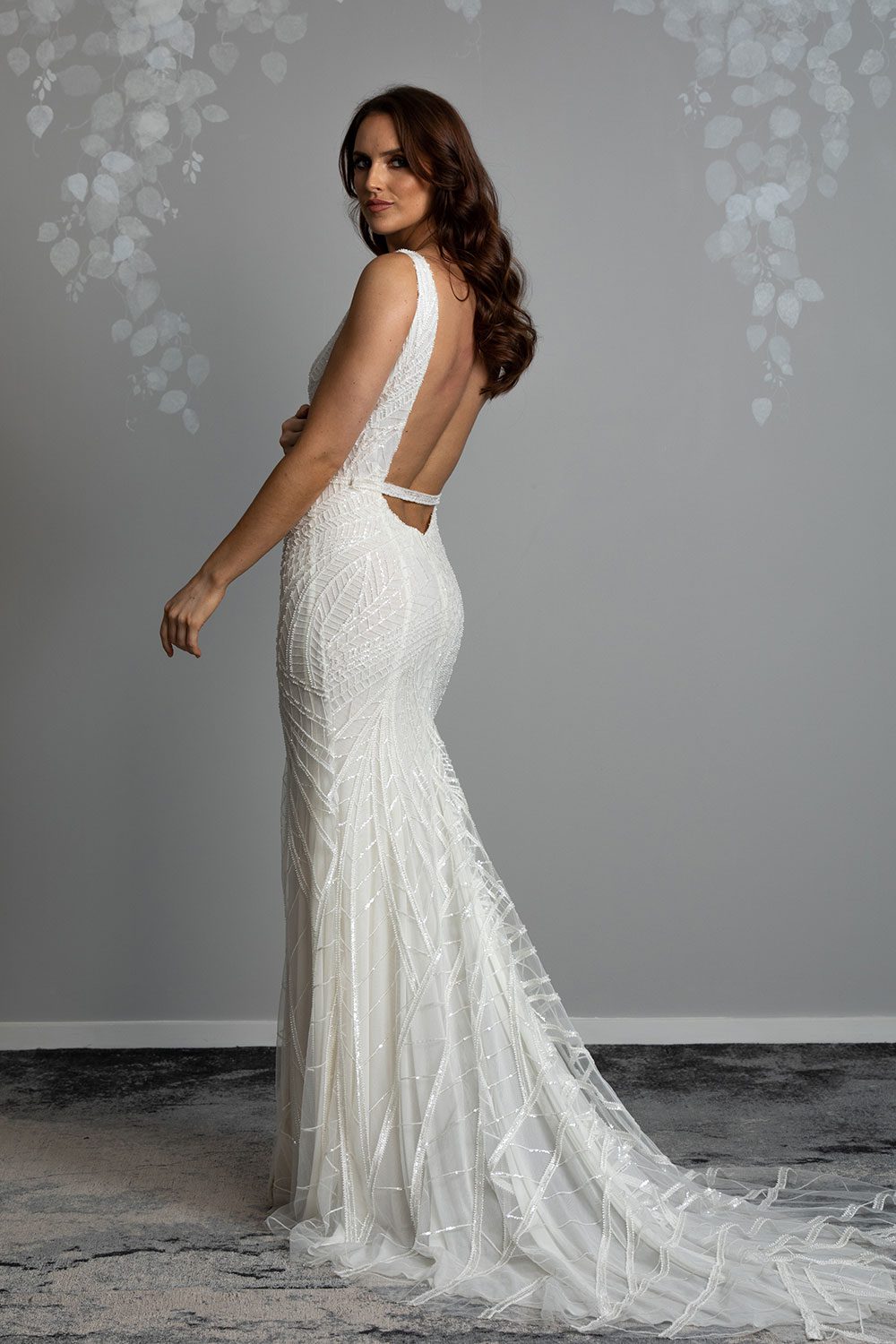 Elle Wedding gown from Vinka Design - Wedding dress with illusion neckline and deep plunge in the front with low back. Stunning beaded embroidery over a stretch base that sculpts and flatters the figure and falls into a beautiful flared train. Semi profile of dress with low back and stunning long train with beaded embroidery throughout