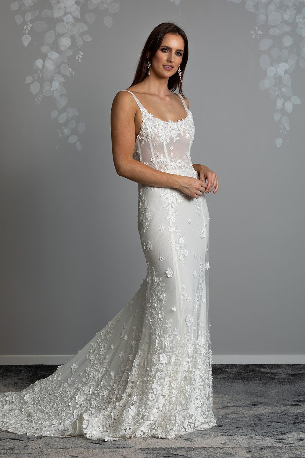 E'more Wedding gown from Vinka Design - This stunning lace wedding gown is hand sewn with a fully beaded 3D flower embroidery. Structured and boned bodice with scoop neckline in the front and low back. Stretch fit skirt flares into full lace train. Full length view of dress showing long train and figure hugging skirt with flattering scoop neck bodice