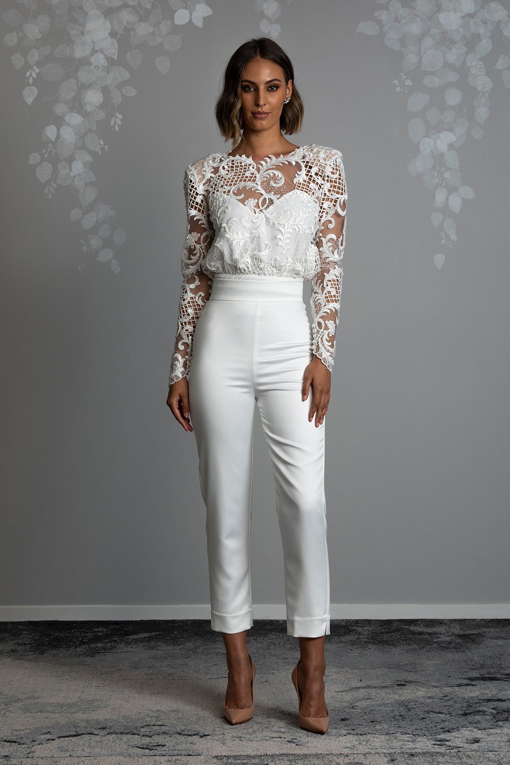 Ava Wedding Trousers and Blouse from Vinka Design - Elegantly tailored trouser combined with a beautiful lace blouse for the Modern Bride. The blouse features a high neck and low back, with in-built camisole, fitted sleeves, & pearl buttons. Model in full front view showing off the beautiful lace blouse with stylish high waisted fitted pants