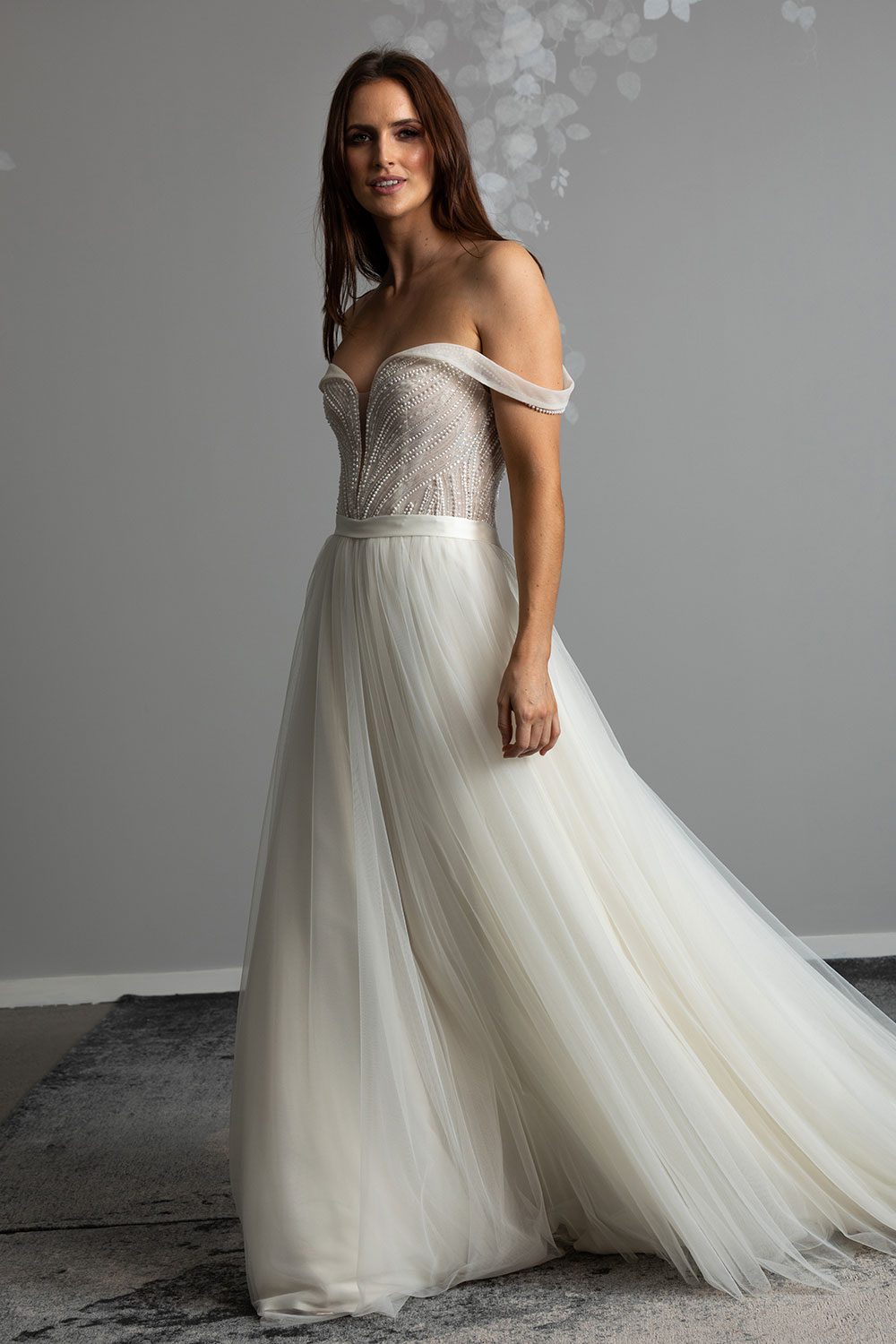 Aroha Wedding gown from Vinka Design - Beautiful & intricate pearl beading is hand-appliqued along this wedding gown’s structured, boned bodice. Delicate off-shoulder straps are complemented by the sweetheart neckline. - 3 quarter view of model showing the skirt made of soft dreamy tulle
