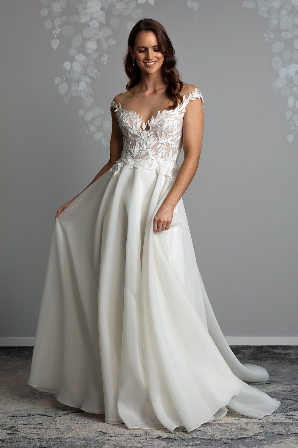 Ariana Wedding gown from Vinka Design - This gorgeous gown features delicate leaf lace hand-appliqued throughout the semi-sheer, structured bodice and up over the shoulder and skirt made of dreamy satin organza layers. Model shows off the light translucent effect of the skirt