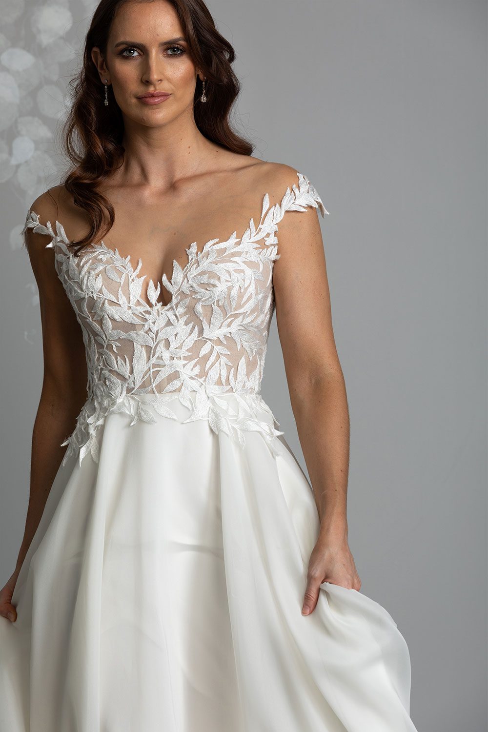 Ariana Wedding gown from Vinka Design - This gorgeous gown features delicate leaf lace hand-appliqued throughout the semi-sheer, structured bodice and up over the shoulder and skirt made of dreamy satin organza layers. Close up of model showing off shoulder leaf lace bodice and soft skirt