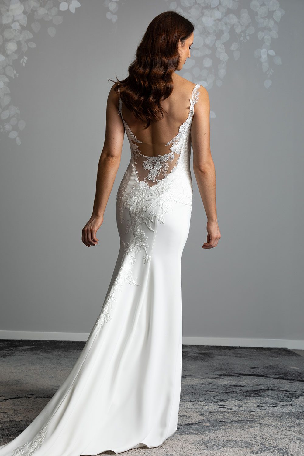 Ana Wedding gown from Vinka Design - This beautiful gown is graced by hand-appliqued delicate floral leaf lace, subtly worked into the front of the bodice and more prominently on the back. A fit-and-flare cut. Model revealing the low back of the gown with intricate lace on illusion tulle