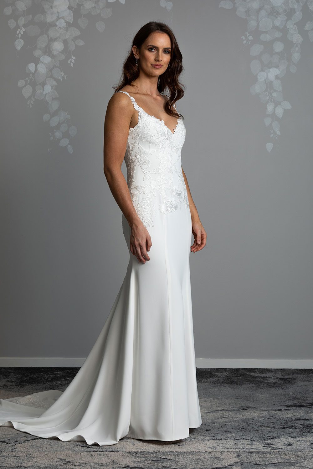 Ana Wedding gown from Vinka Design - This beautiful gown is graced by hand-appliqued delicate floral leaf lace, subtly worked into the front of the bodice and more prominently on the back. A fit-and-flare cut shapes the figure. Profile of front of the gown with intricate lace detailing and sculpted panels leading to a long train