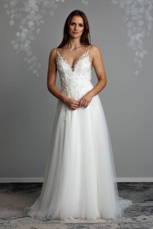 Monique Wedding gown from Vinka Design - This beautiful A-line gown is made with stunning 3D floral lace. Full length view of model with hands clasped wearing beautiful 3D floral lace bodice with low V neckline and long tulle and lace skirt with flared train