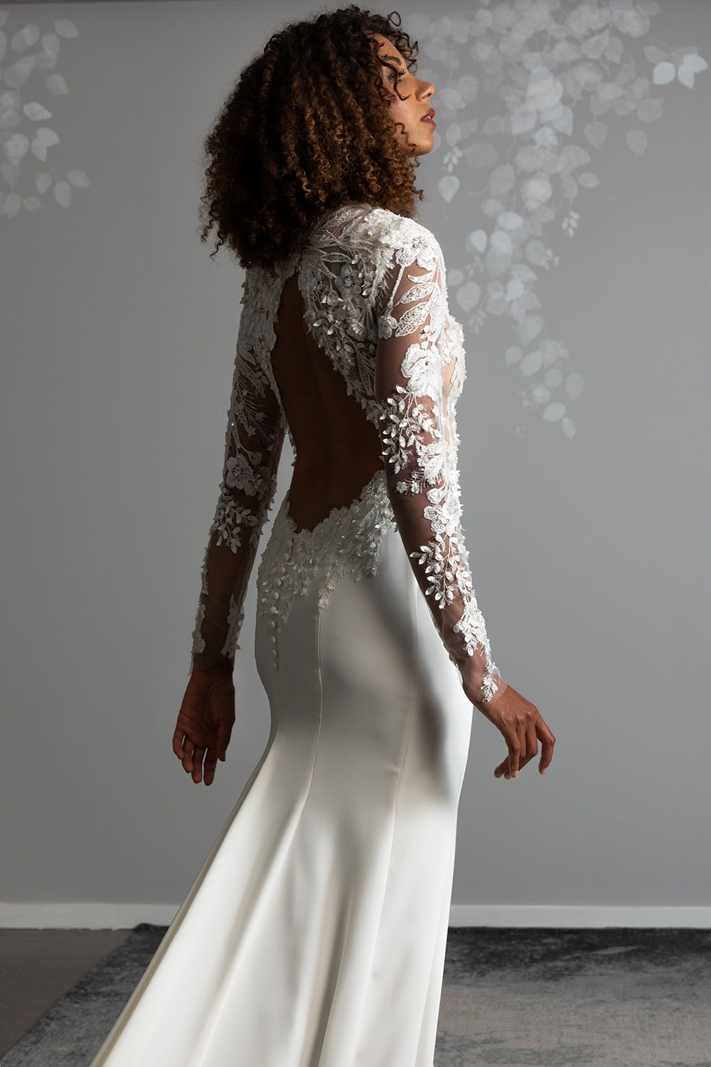 Moana Wedding gown from Vinka Design - Spectacular wedding dress perfect for the modern bride who still wants a classic spark! 3D lace embroidery complemented by a high neckline, fitted sleeves, and stunning low back into a flare train. Close up of low back with 3D lace embroidery and long sleeves