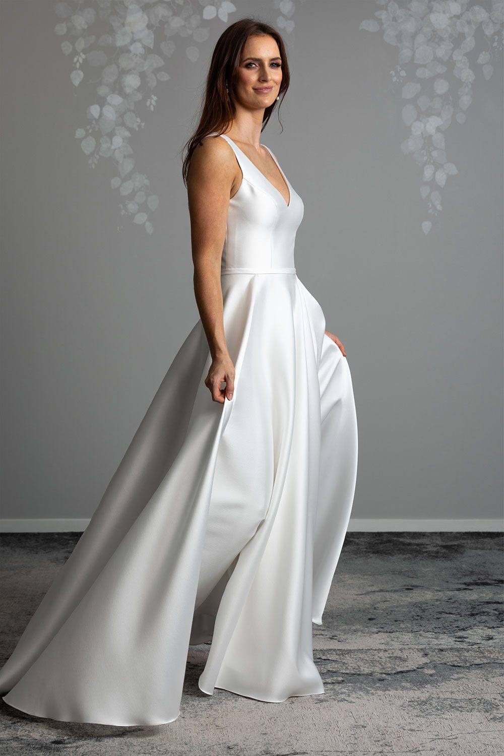 FlMadison Wedding gown from Vinka Design - This gown is both classic and contemporary, made beautifully with luxurious Mikado satin. The bodice is structured with a deep V-neckline and a squared, low back. Model showing profile view of gown highlighting the full skirt with irregular folds and fun and versatile pockets that fall elegantly into a sweeping train